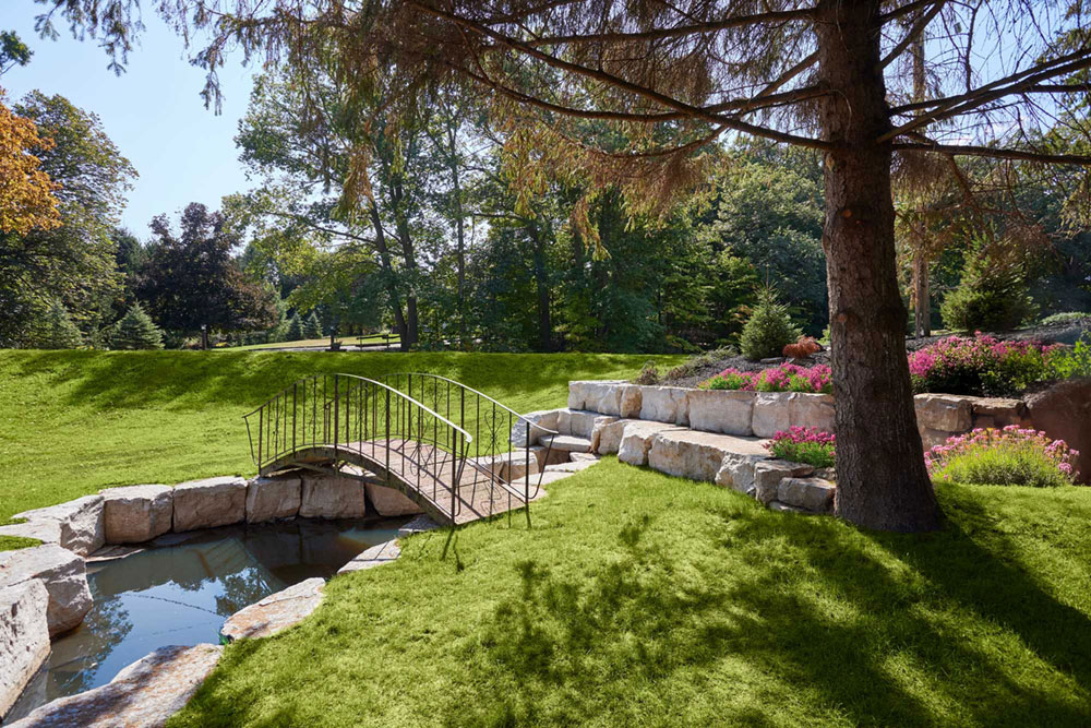 A wood bridge over an armour stone, high flow managing water channel that feeds into a landscaped fishpond.