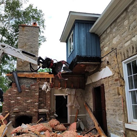 Demolition service in progress as an excavator demolishes a structurally unsafe section of an old house.