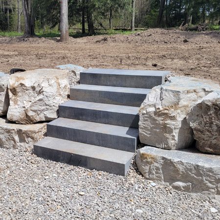 Landscape improvements service in progress with hardscape, including armour stone, steps and gravel.