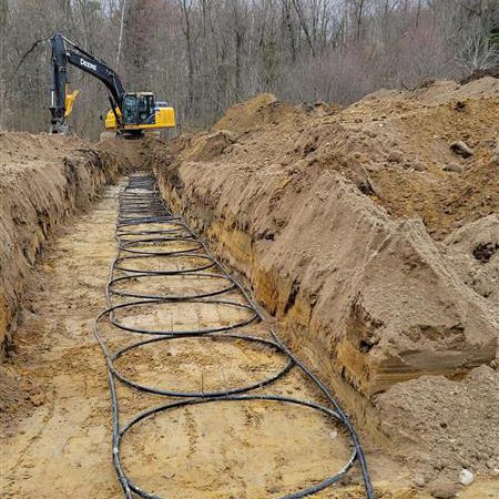 An excavation contractor performs site work services, including digging trenches and installing horizontal geothermal ground loops to support a residential ground source heat pump.