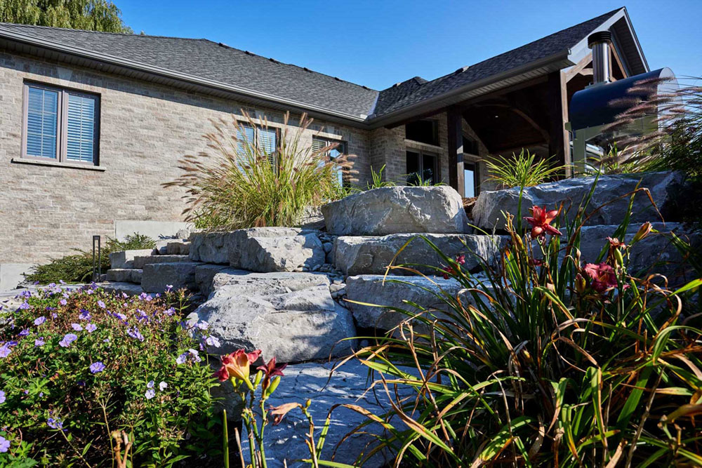 A stunningly landscaped outdoor patio with armour stone framed gardens.